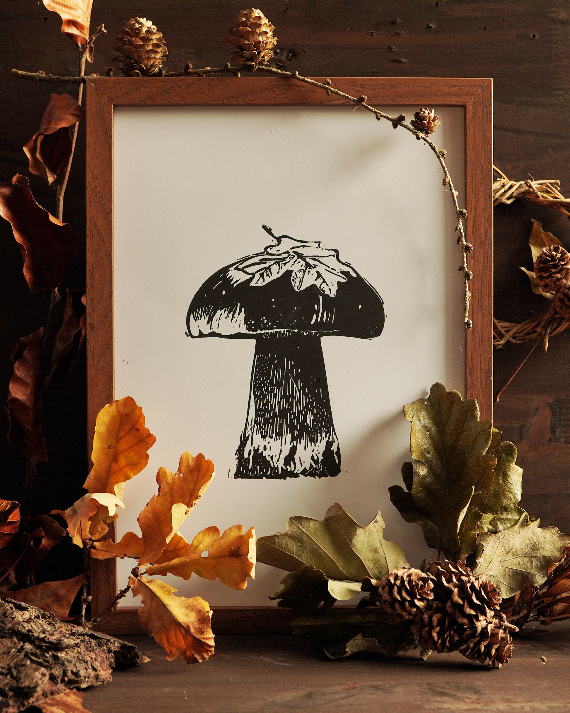 Linocut print of a boletus surrounded by autumn leaves.