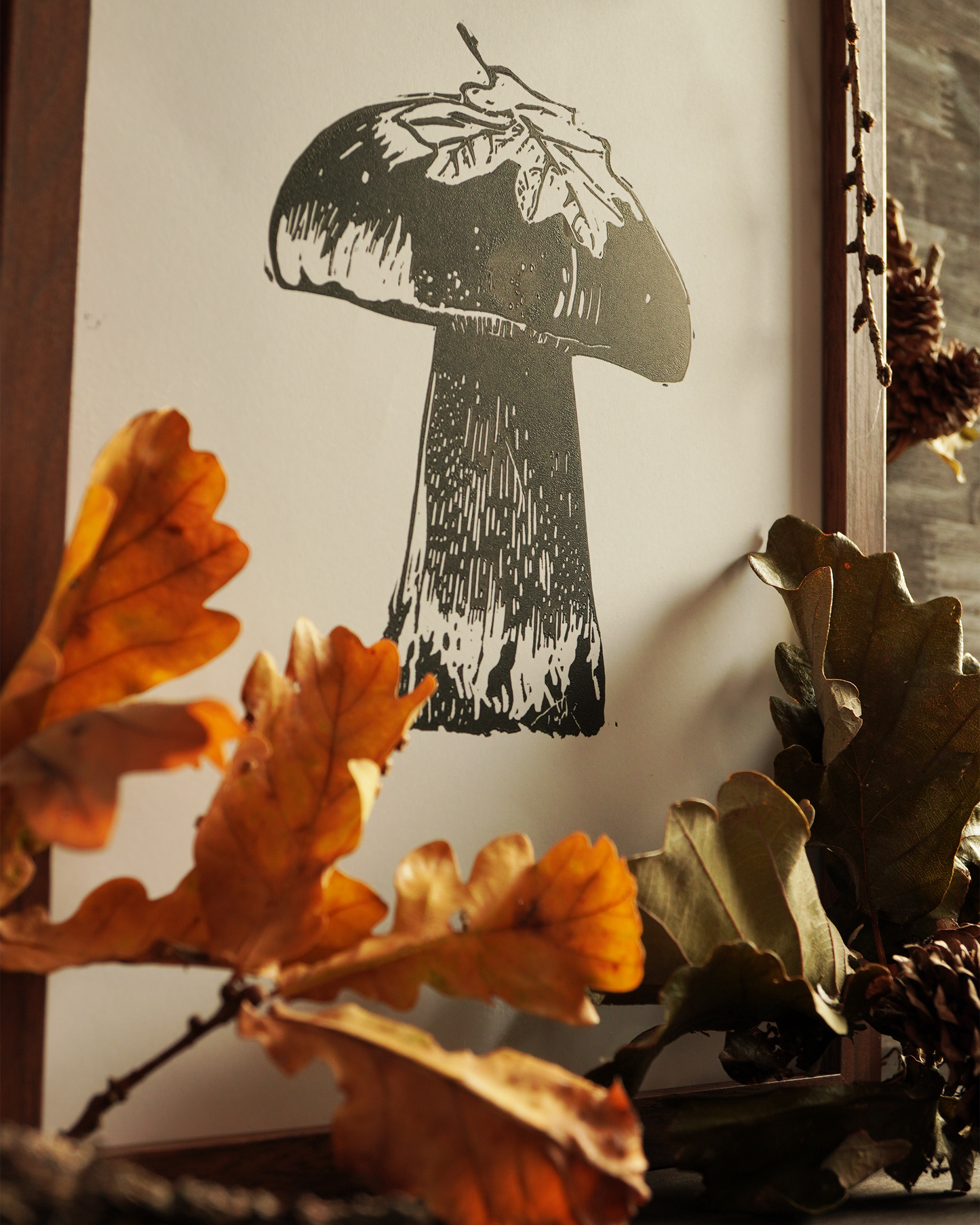 Linocut print of a boletus surrounded by autumn leaves.