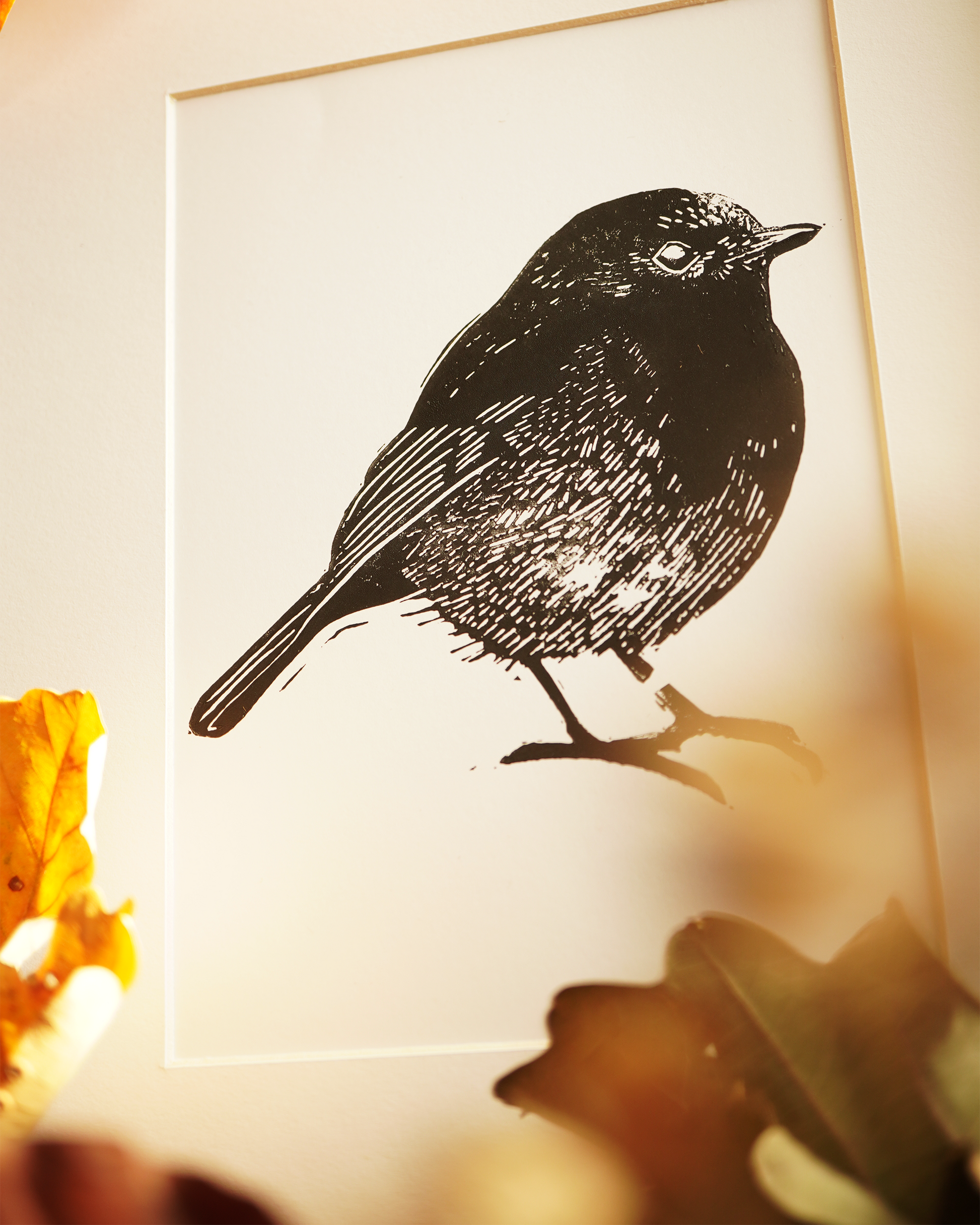 Linocut print of a robin bird surrounded by autumn leaves.