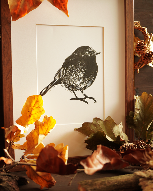 Linocut print of a robin bird surrounded by autumn leaves.