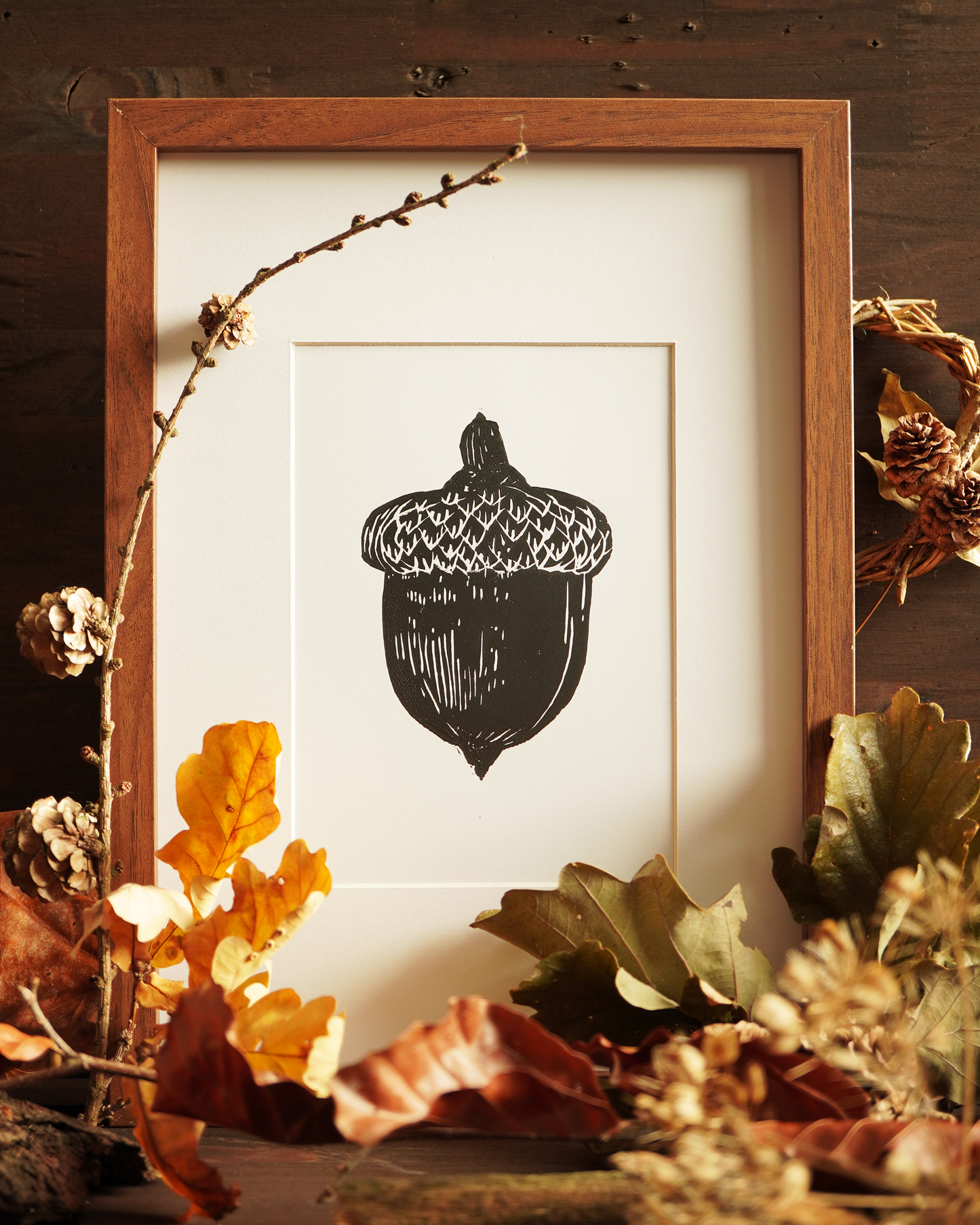 Linocut print of an acorn surrounded by autumn leaves.