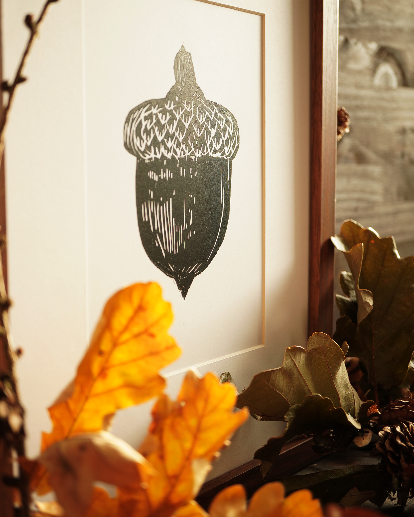 Linocut print of an acorn surrounded by autumn leaves.