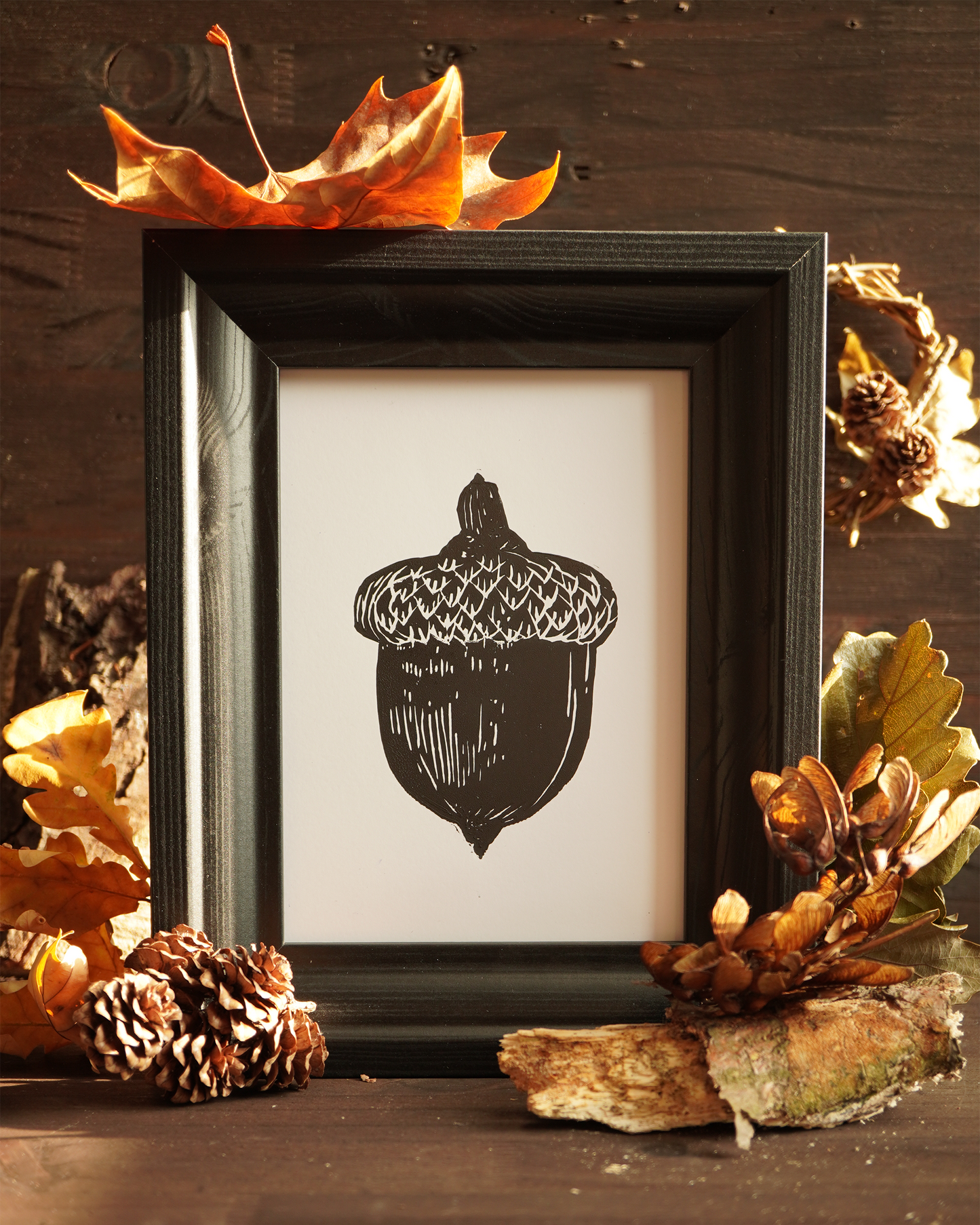 Linocut print of an acorn surrounded by autumn leaves.