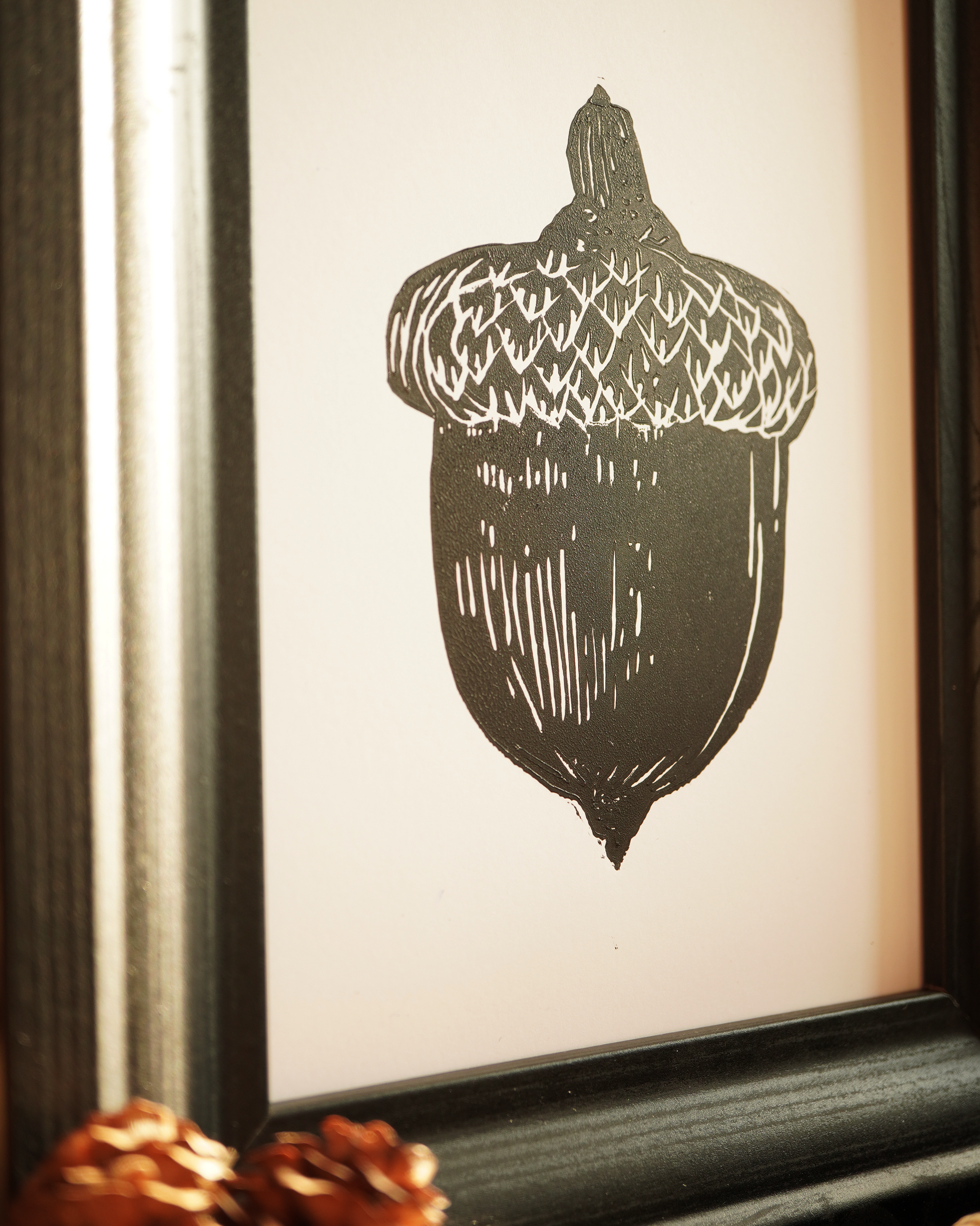 Linocut print of an acorn surrounded by autumn leaves.