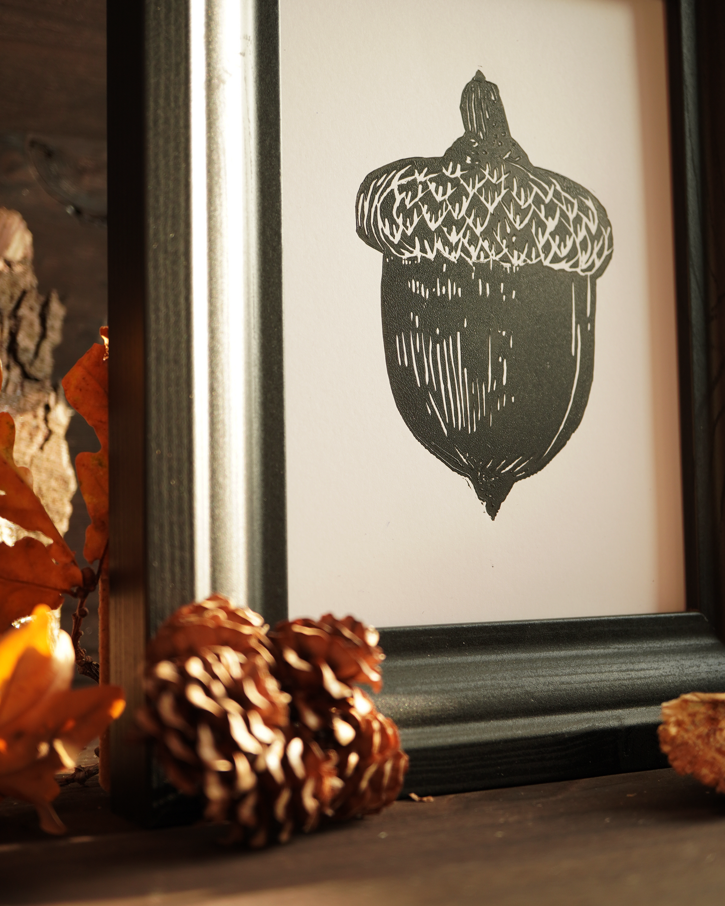 Linocut print of an acorn surrounded by autumn leaves.