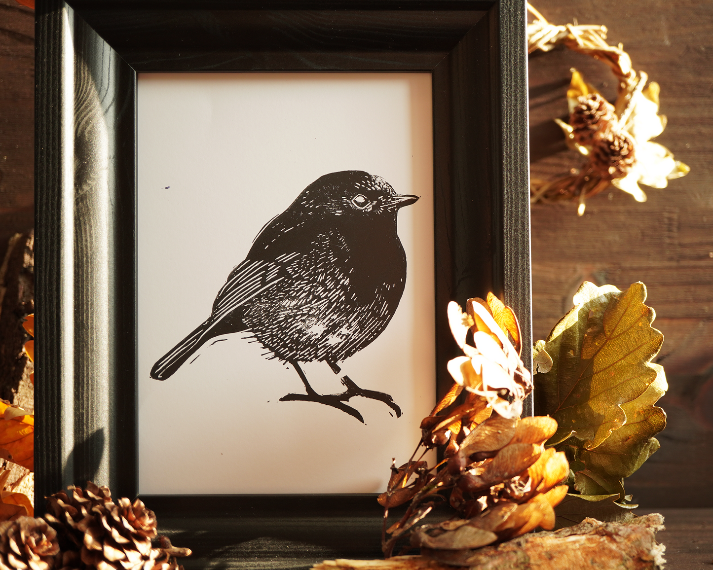 Linocut print of a robin bird surrounded by autumn leaves.