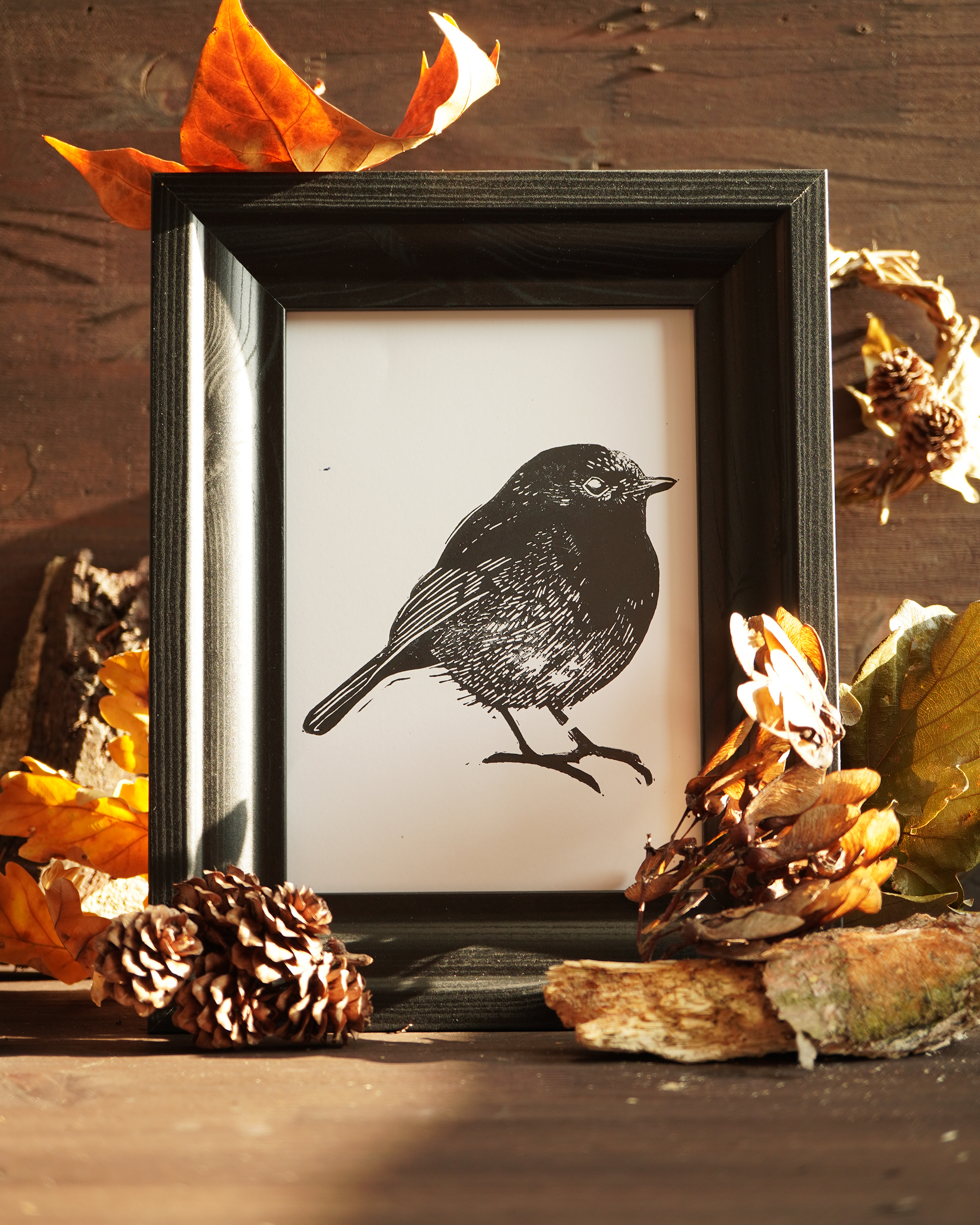 Linocut print of a robin bird surrounded by autumn leaves.