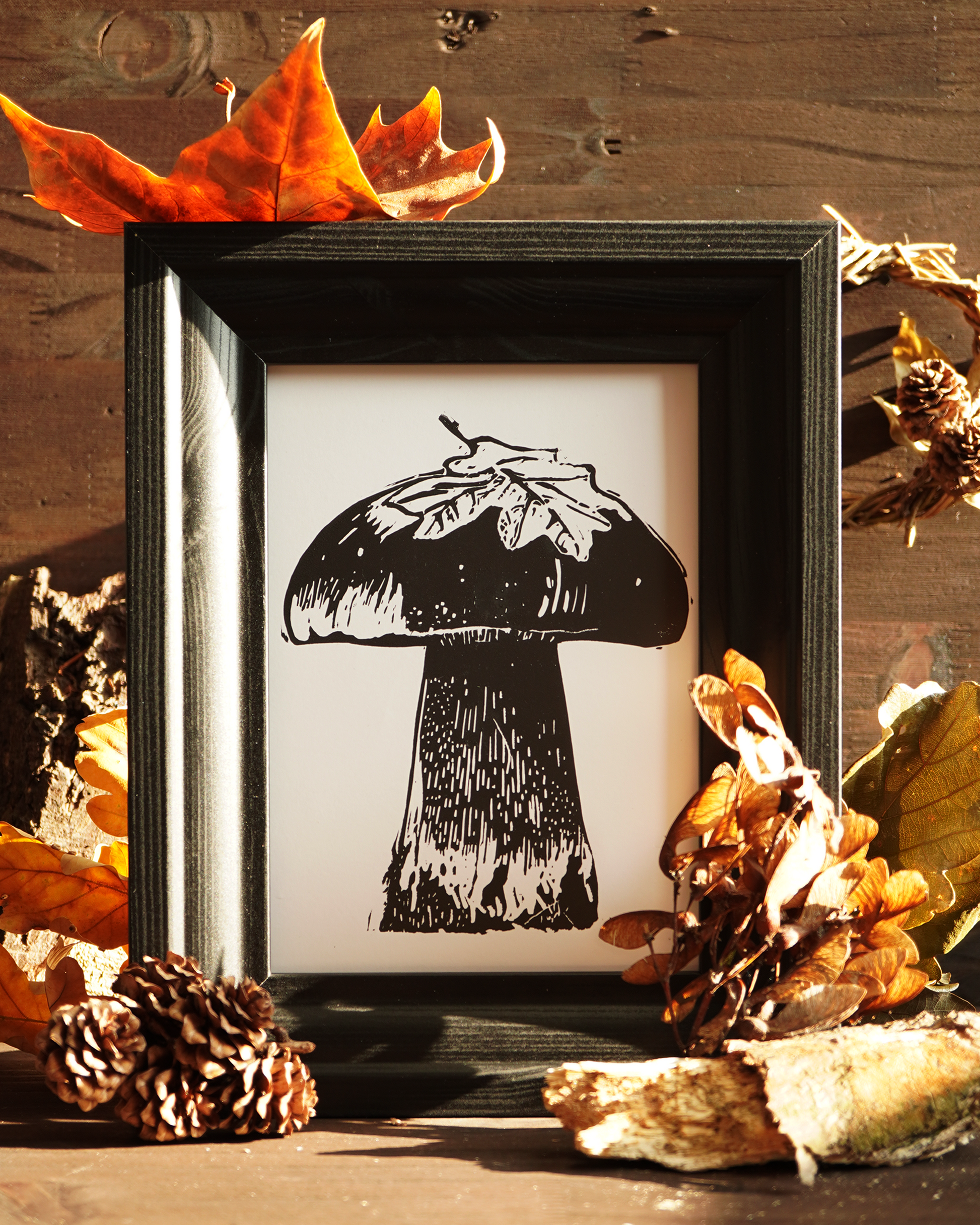 Linocut print of a boletus surrounded by autumn leaves.