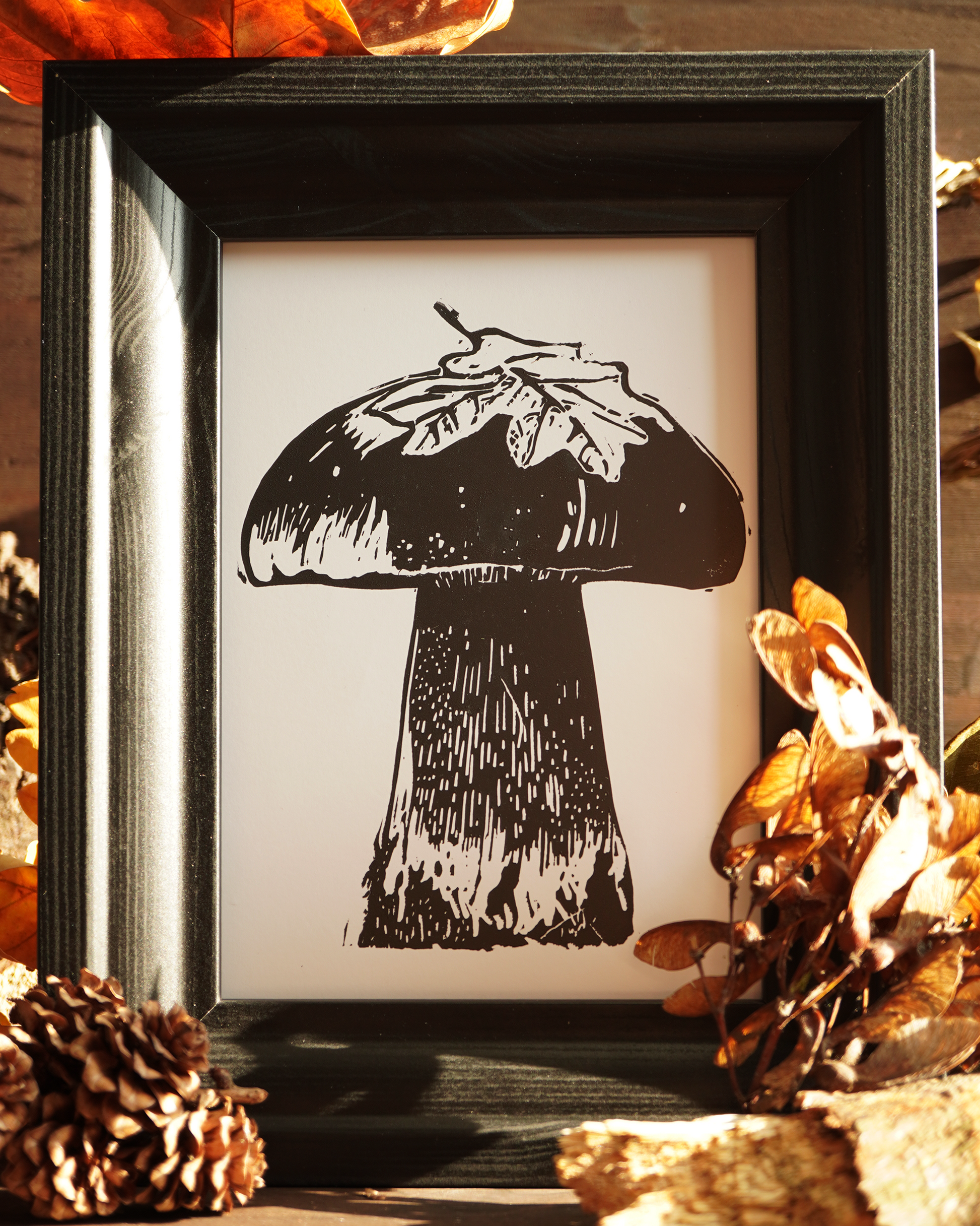 Linocut print of a boletus surrounded by autumn leaves.